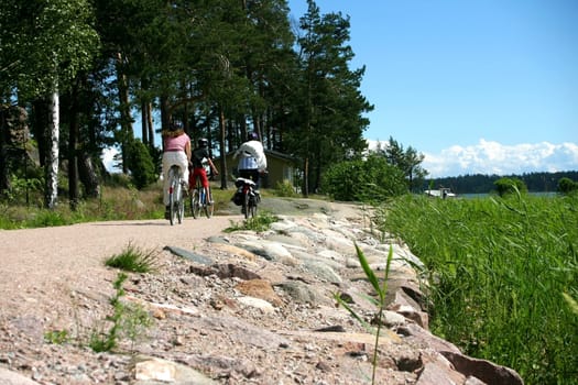 Family on a bike trip, next to the sea, on a gravel road at summer