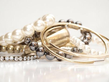 Pearls and earrings in assorted colors in a pile, on white background with reflection 