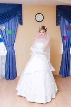 a bride waits for her groom in her house, standing between the two windows