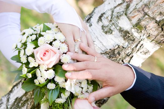 two hands of bride and groom over a wedding bouquet