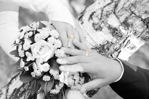 hands of the bride and groom over the flower bouquet in black and white