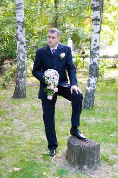 groom with a flower bouquet waits for his bride in the park