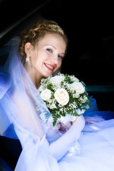 happy bride with a rose bouquet in the car