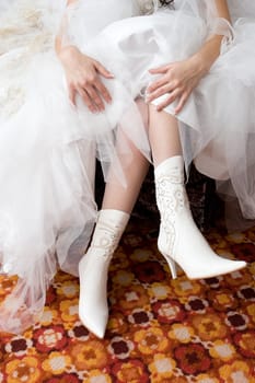 hands of the girl in a white wedding dress put on the white boots