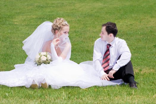 a bride and a groom siting on the grass and looking to the eyes of each other