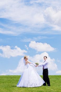 Newly-married couple on a green grass under the blue sky