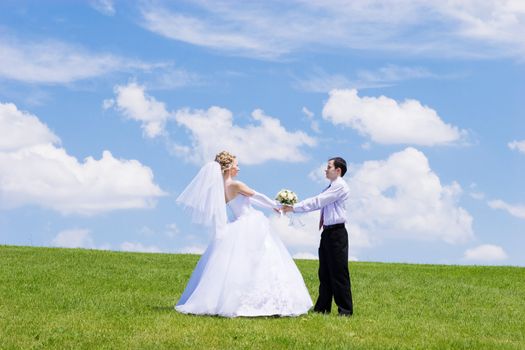 Newly-married couple on a green grass under the blue sky