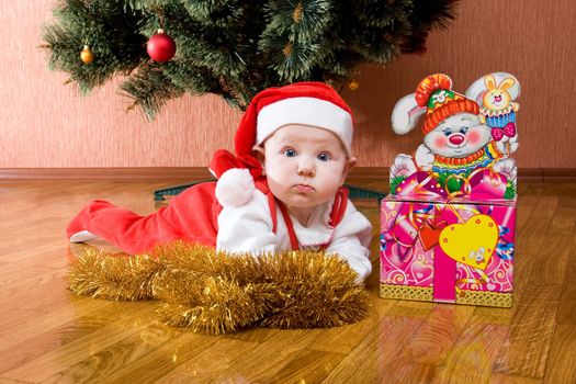 Little baby as Santa in red cap laying on the floor with gifts