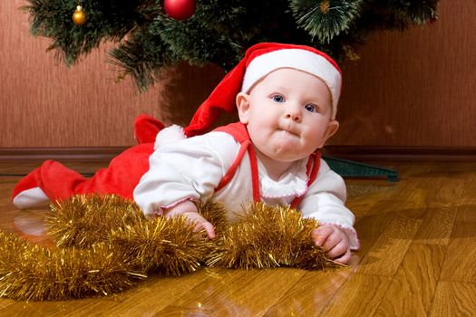 Little baby as Santa in red cap laying on the floor with gifts