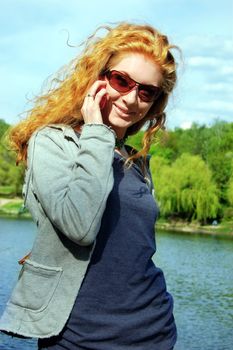 Cheerful girl smiling and talking on phone on nature background