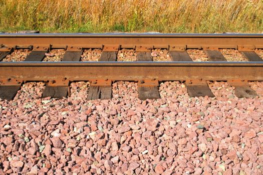 Rail tracks between grass and gravel in a rural area.