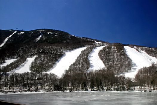 Many ski slopes in winter with frozen lake at bottom.