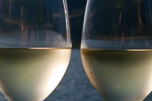 Closeup of two galsses filled with white wine with a lake in the background