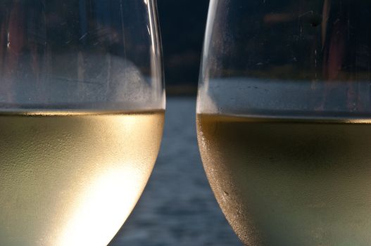 Closeup of two galsses filled with white wine with a lake in the background