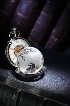 Closeup of glass globe and vintage pocket watch on dark background with old books