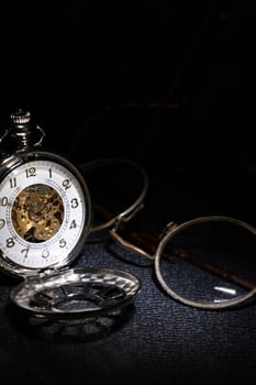Closeup of vintage pocket watch near spectacles on dark background