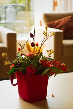 Backlight image of interior with mixed bouquet of yellow, red and orange flowers in beautiful little bag on a table