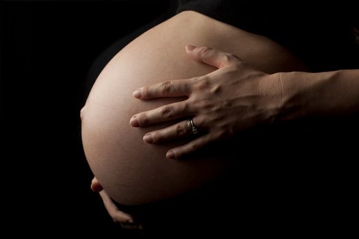 close up of a pregnant womans stomach, isolated on black background.