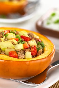 Stuffed baked pumpkin filled with zucchini, red bell pepper, minced meat, onions and garnished with parsley (Selective Focus, Focus one third into the stuffing)