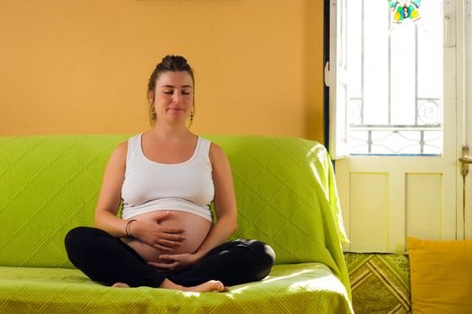 Pregnant woman meditating while sitting on a sofa