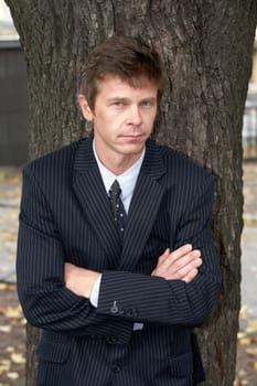 Man leaning against tree in city, arms crossed