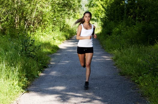 young woman jogging in the park in summer, trees and grass background