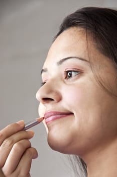Pretty young Indian woman applying cosmetics on lips