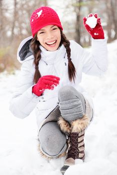winter woman playing in snow throwing snowball at camera smiling happy having fun outside on snowing winter day. Beautiful joyful multicultural Asian Caucasian girl outdoors.