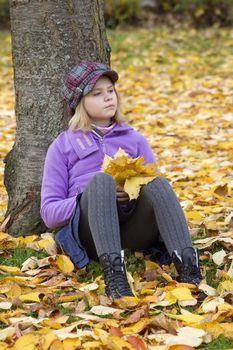Full length portrait of a little girl sitting under tree in autumn park