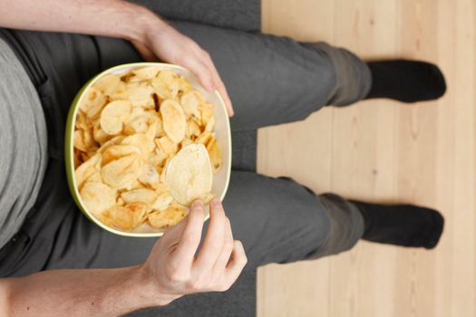 A man on a couch eating potato chips