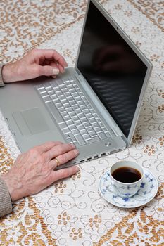 Senior using computer and drinking coffee