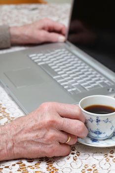 Senior using computer and drinking coffee