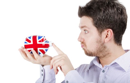 Isolated photograph of a blonde British man playing with a piggy bank with UK flag.