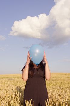 Young woman, dressed with black dress, holding blue balloon in front of her face.