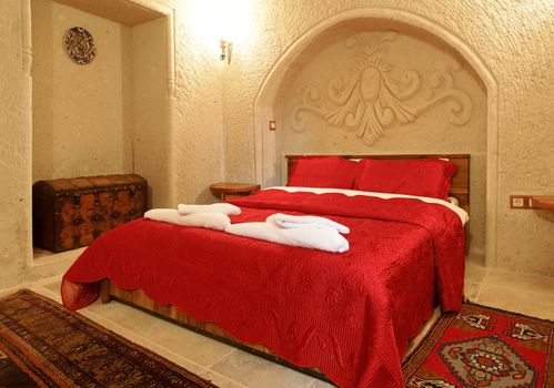 interior architectural detail of bedroom with alcove and archway with detailing, bed cover in embroidered bright red bedspread and pillow cases, treasure chest shipping trunk, woven mats and wall light. Landscape with crop area and copy space.