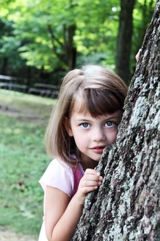 Little girl leaning against a large oak tree and looking at the viewer.