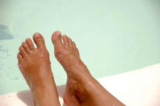 Feet by the pool side is being refreshed by cool water drops. The water drops are in motion blur.