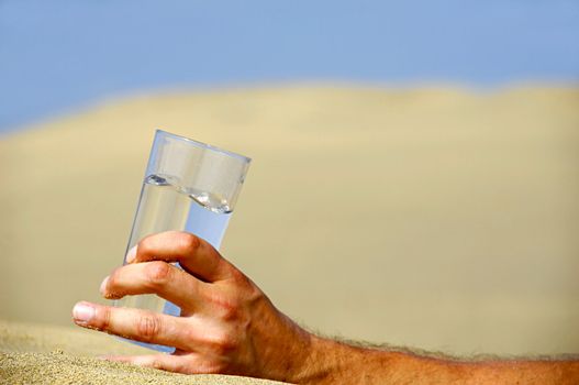 Hand is holding a fresh glass of cold water in desert.