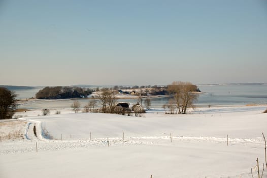 Idylic winter landscape with, fram, fields and frozen sea.
