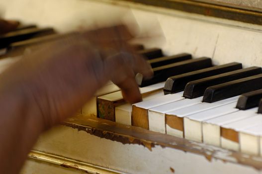 Musician is playing on a very old piano. Noate that the hand and fingers are in motion blur