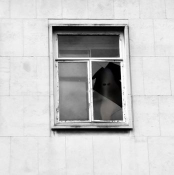 A view of a a derelict building with a ghost looking out of a broken window.