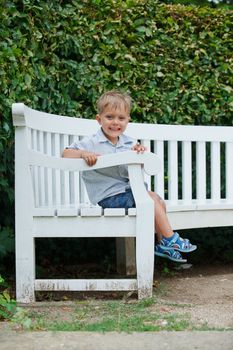 Cute little boy sits on a bench in a park. Vertical view