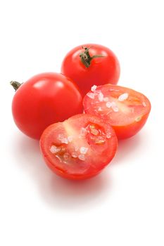 A few cherry tomatoes. One of them is cut and it is salt. On a white background.