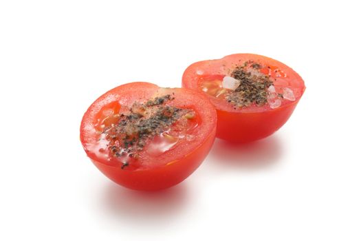 A few cherry tomatoes. One of them is cut and it is salt and pepper. On a white background.