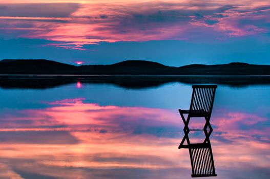 Scenic view of sunset over inlet and hills with a chair in the calm water, with reflections of sunset and chair. Symbolizing peace, loneliness or emptyness