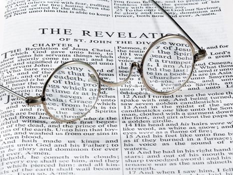 Old fashioned round reading glasses laying on a page from the bible on the revelation
