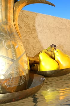 Brass olive oil decanter and a brass fruit bowl on a glass table.