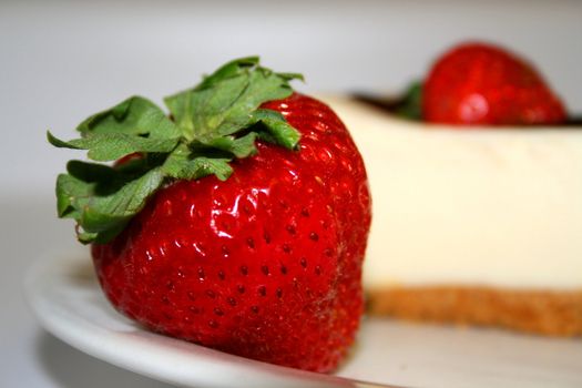 Close up of a strawberry and a cheesecake on a plate with a white background.