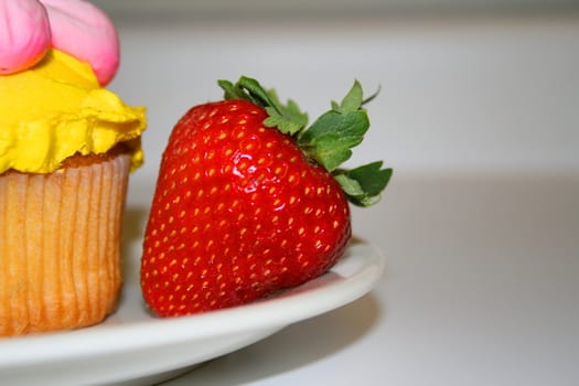 Strawberry and a muffin with cream vivid frosting on a plate.