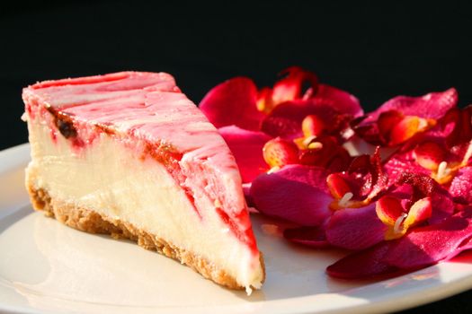 Strawberry cheesecake and pink orchids on a plate with black background.